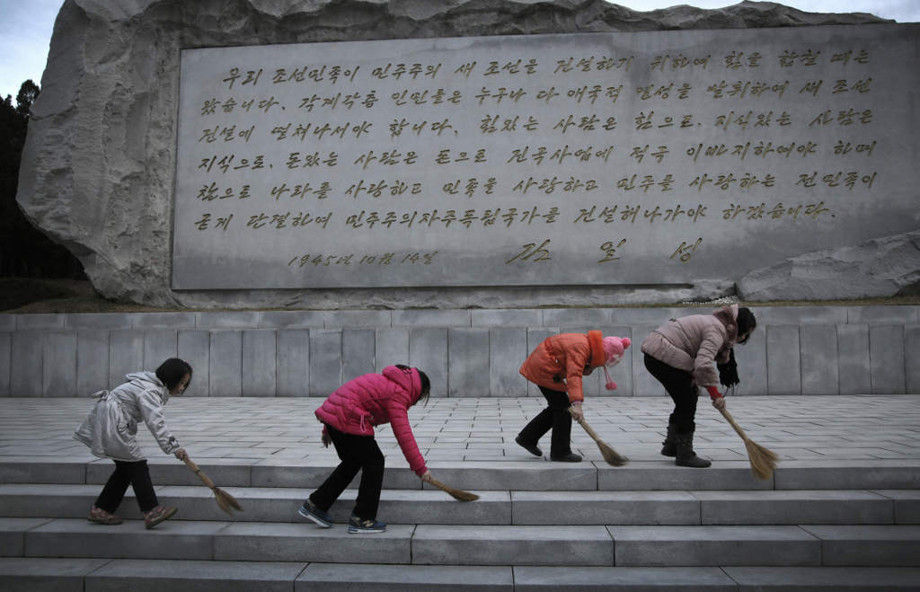 Skolflickor sopar marken framför en stenvägg som pryds av ett citat från Kim Il-Sung, tisdagen den 1 december 2015. Foto: Wong Maye-E