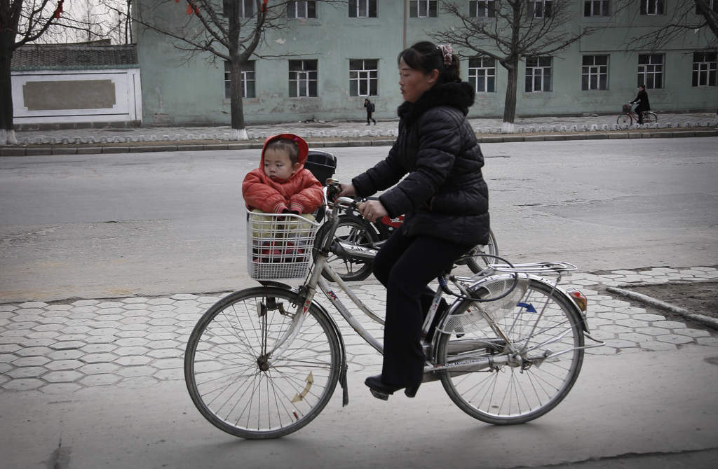 En nordkoreansk kvinna cyklar med ett barn i cykelkorgen, den 22 februari 2016 i Kaesong. En industipark i Kaesong som Nord- och Sydkorea drivit gemensamt stängdes ner 2016 efter Nordkoreas kärnvapen- och robottester. Foto: Wong Maye-E/AP